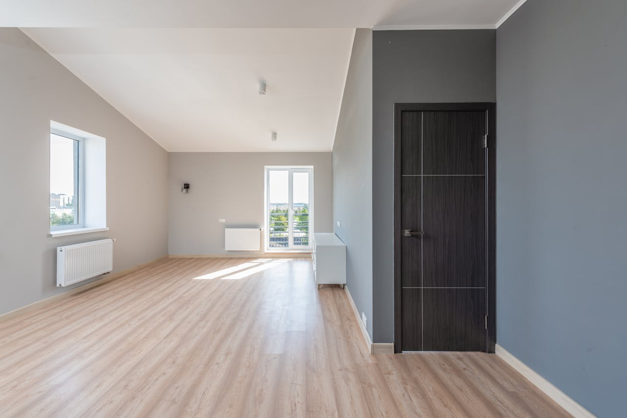 Spacious empty room with wooden flooring and large windows for ample natural light.